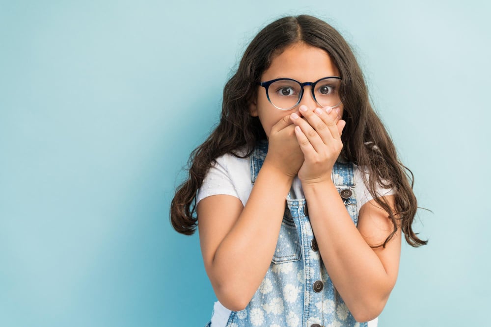 Free photo hispanic girl in shock covering mouth with hands while making eye contact against plain background
