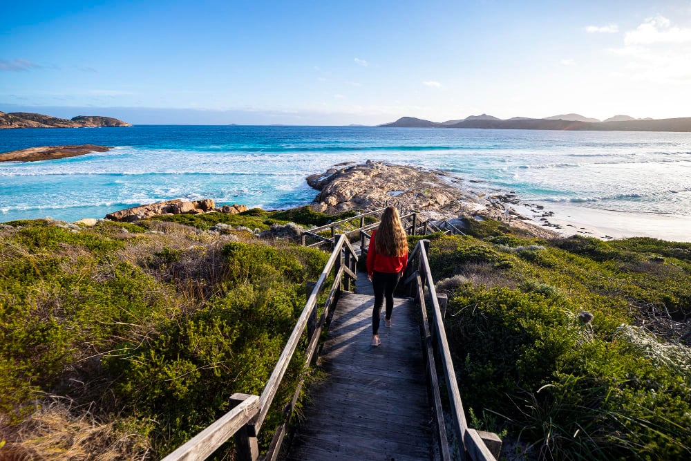 Photo beautiful long-haired girl walks down stairs to paradise beach, sunset on lucky bay beach