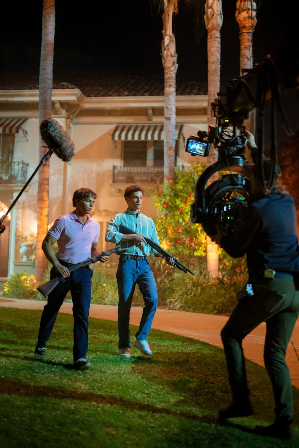 Behind-the-scenes image from
Cast of Monsters The Lyle and Erik Menendez Story, showing two characters with rifles, along with the film crew, illustrating the intensity of the production.