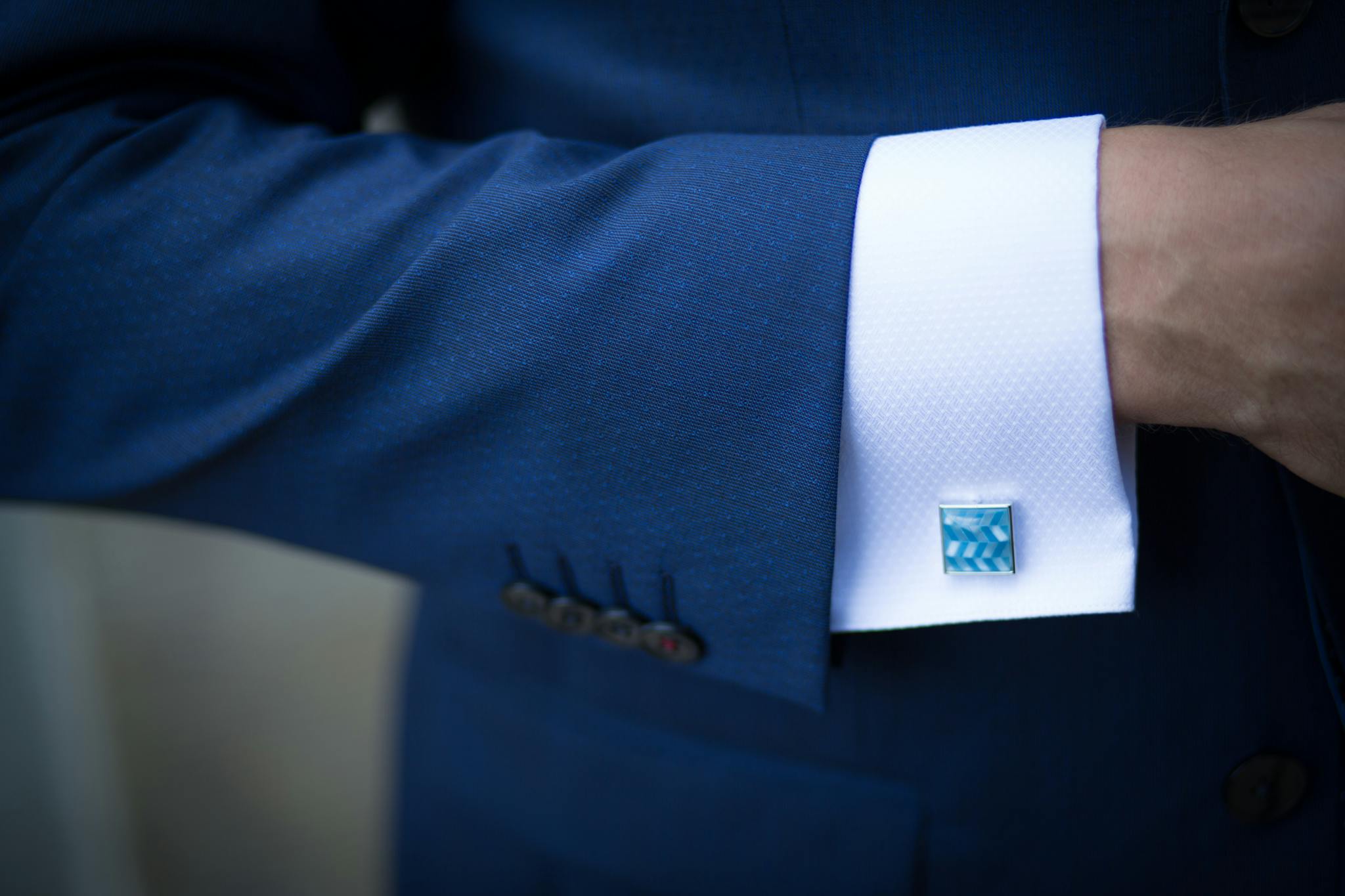Close-up of a blue suit sleeve with decorative cufflinks, showcasing elegance.