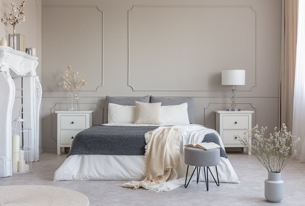 Flowers on white wooden nightstand table in luxury bedroom interior with king size bed