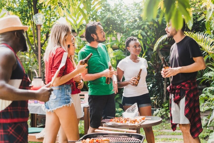 Group of diverse people having barbecue/barbeque party at home, cooking grilled meat/beef for lunch, happy friends party life