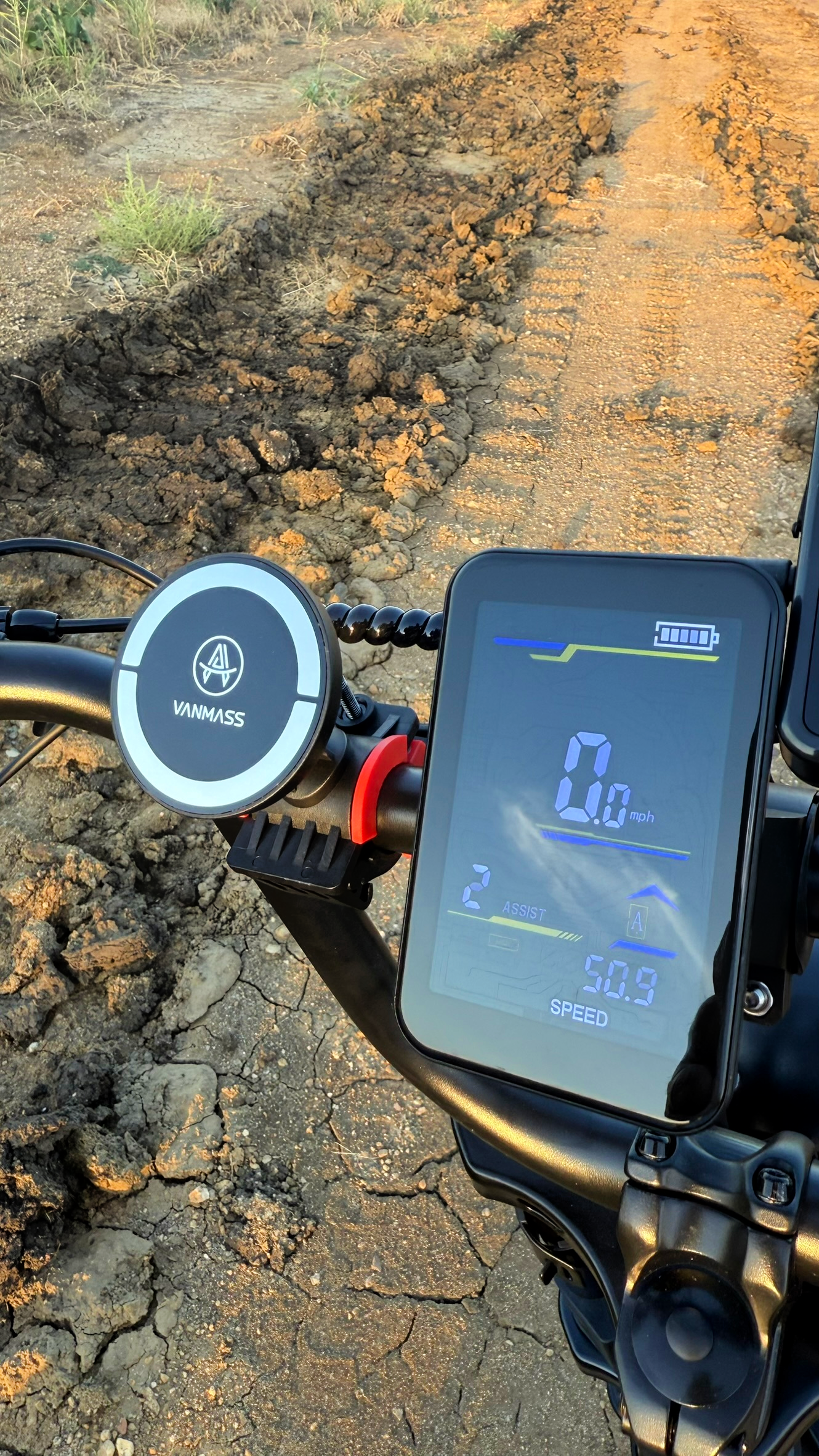E-bike handlebar with LCD speedometer and VANMASS magnetic phone mount on a dirt trail.