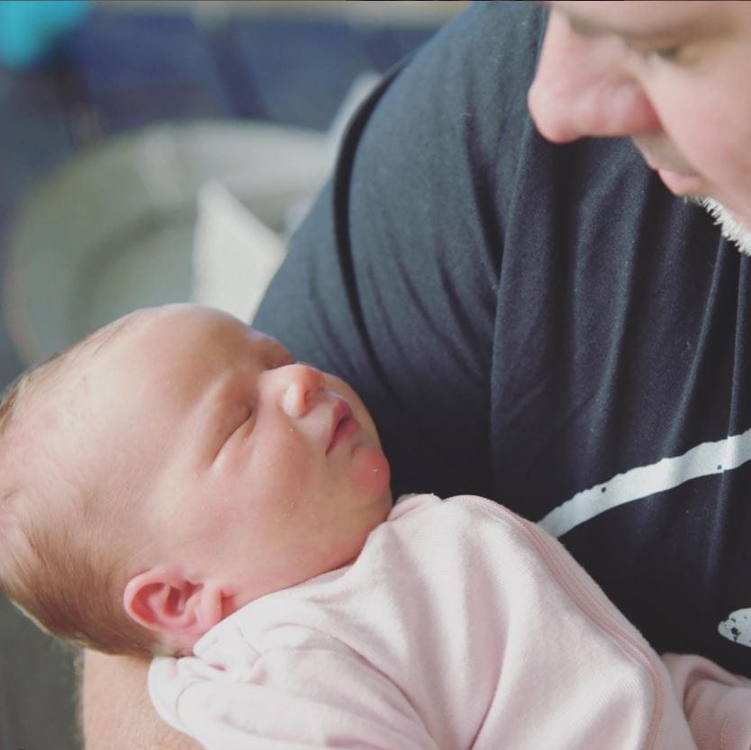 Close-up of father tenderly looking down at sleeping newborn baby he's holding, capturing quiet moment of new fatherhood