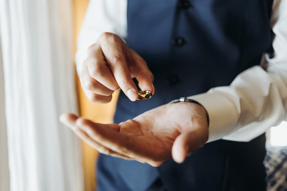 Groom holds wedding ring standing before the window in a hotel r

