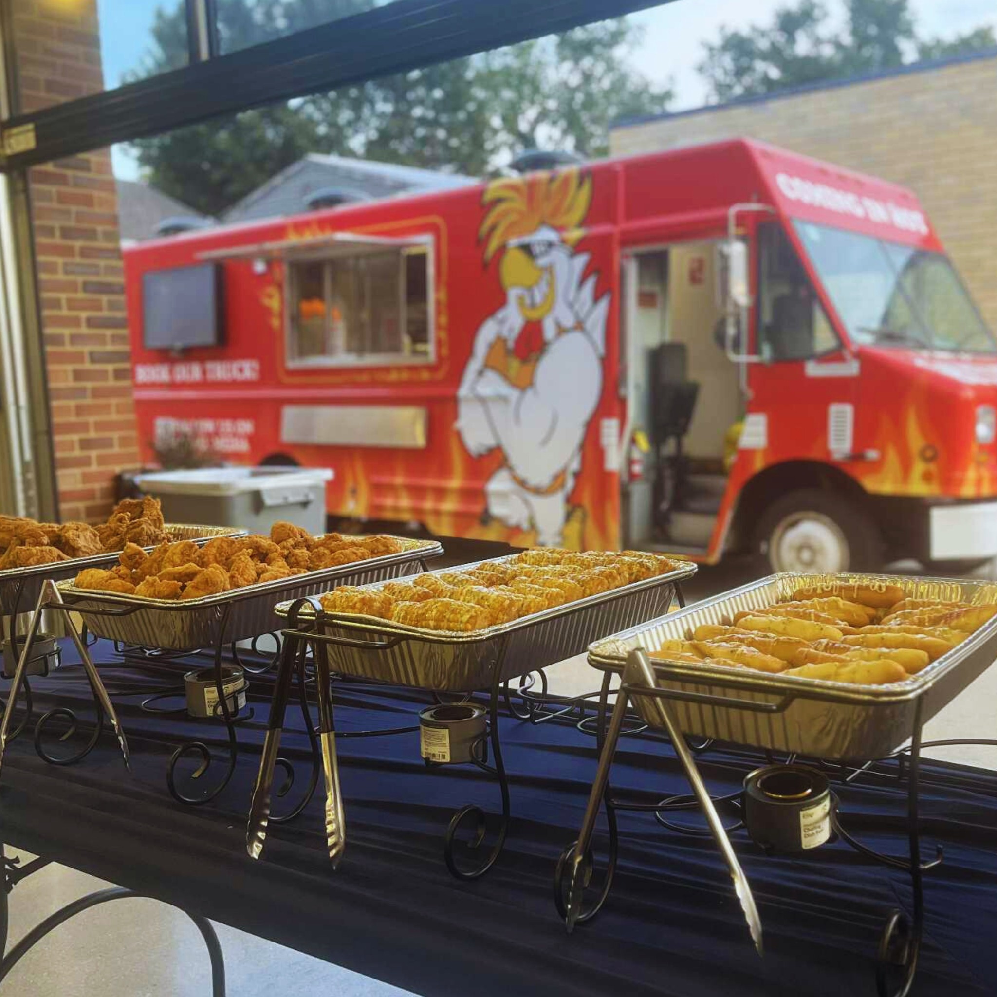 Heaterz Hot Chicken food truck outside with catering trays of crispy chicken and sides set up indoors.