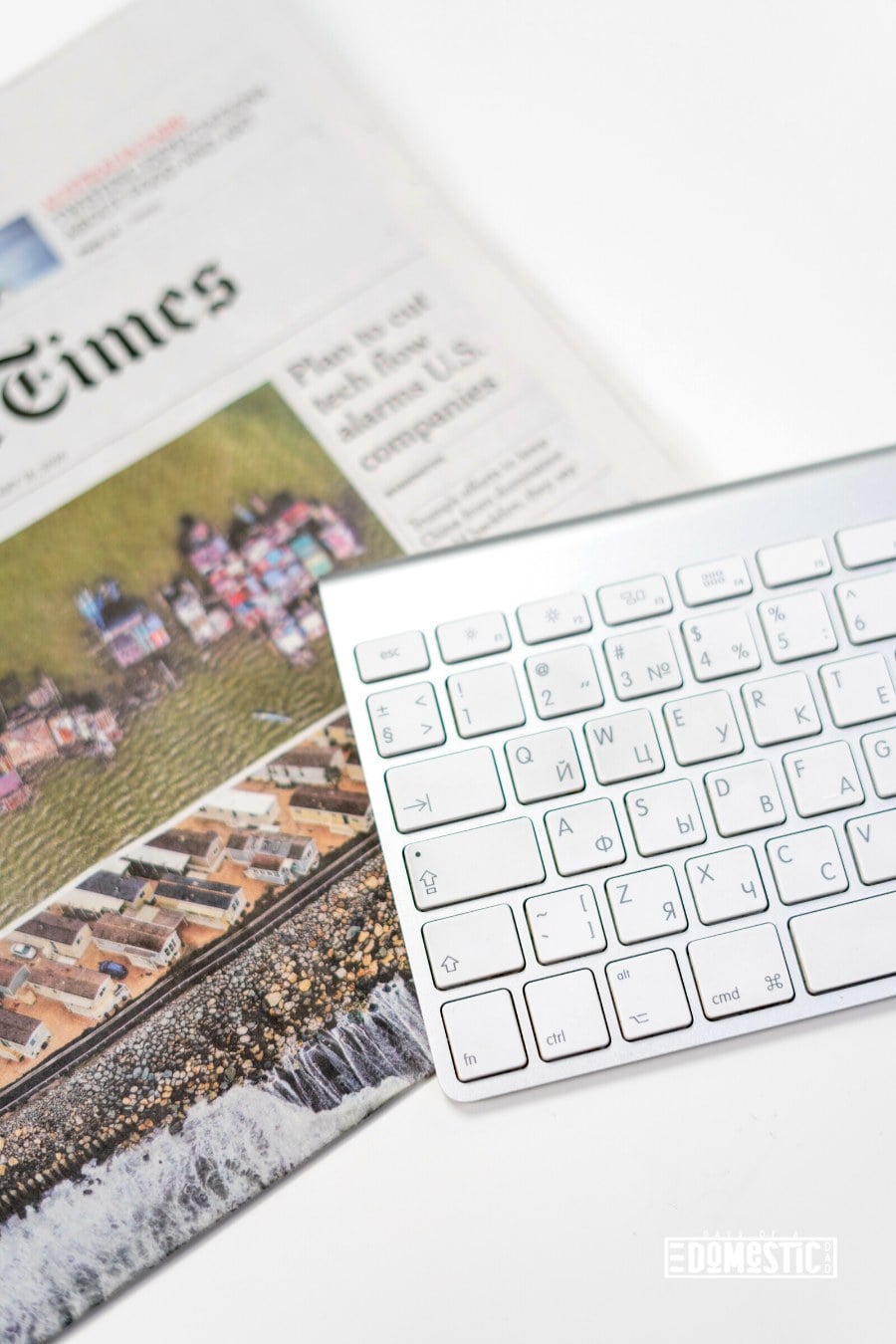 newspaper laying underneath a white computer keyboard