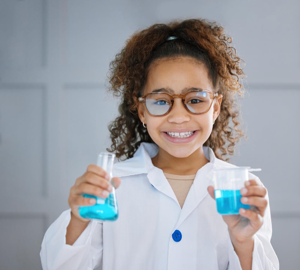 Photo how would you react. cropped portrait of an adorable little girl wearing a labcoat while holding two containers of blue liquid.