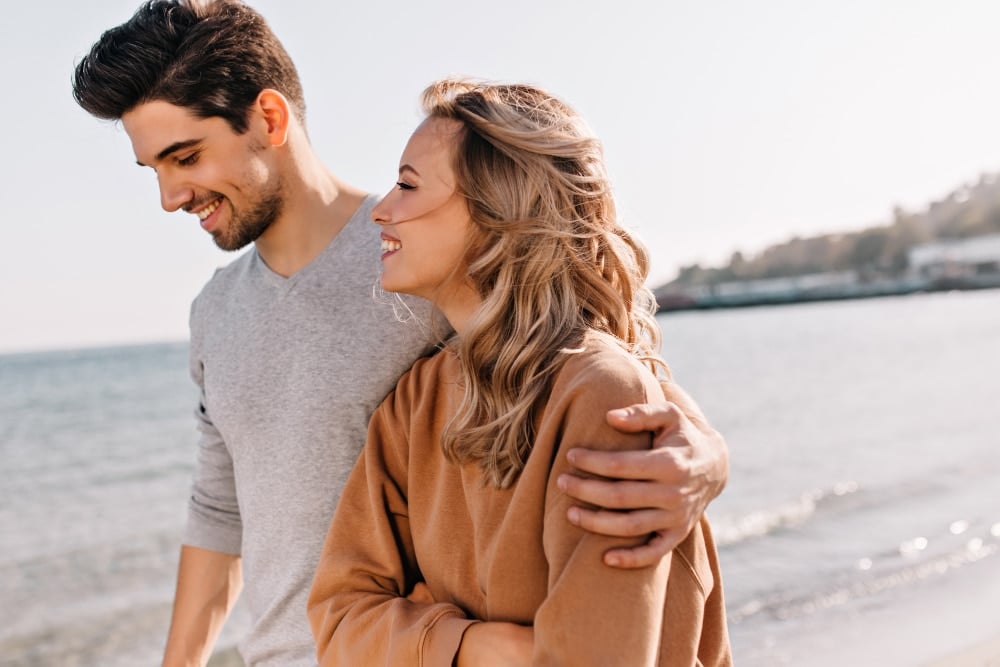 Inspired young man embracing girlfriend during walk at beach. curious blonde woman spending weekend at sea.
