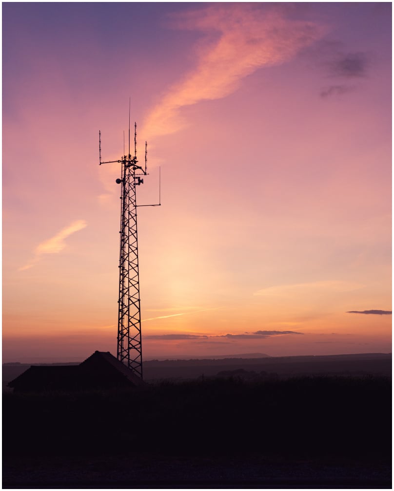 Cell tower standing tall against a colorful sunset sky, illustrating the opportunity to lease your land for cell towers and generate passive income.