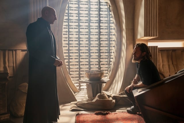 This image captures Mark Strong as Emperor Corrino, engaging in a tense conversation. The lighting and environment reflect the mysterious and authoritarian atmosphere of the Imperium.