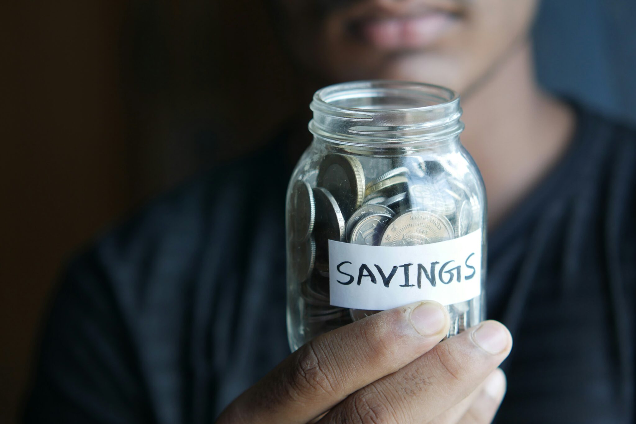 man holding a jar of coins with a white lable savings