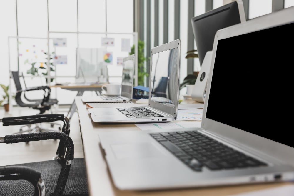 Photo selective focus on laptops sitting on conference table in meeting room office with multiple glass windows in background.