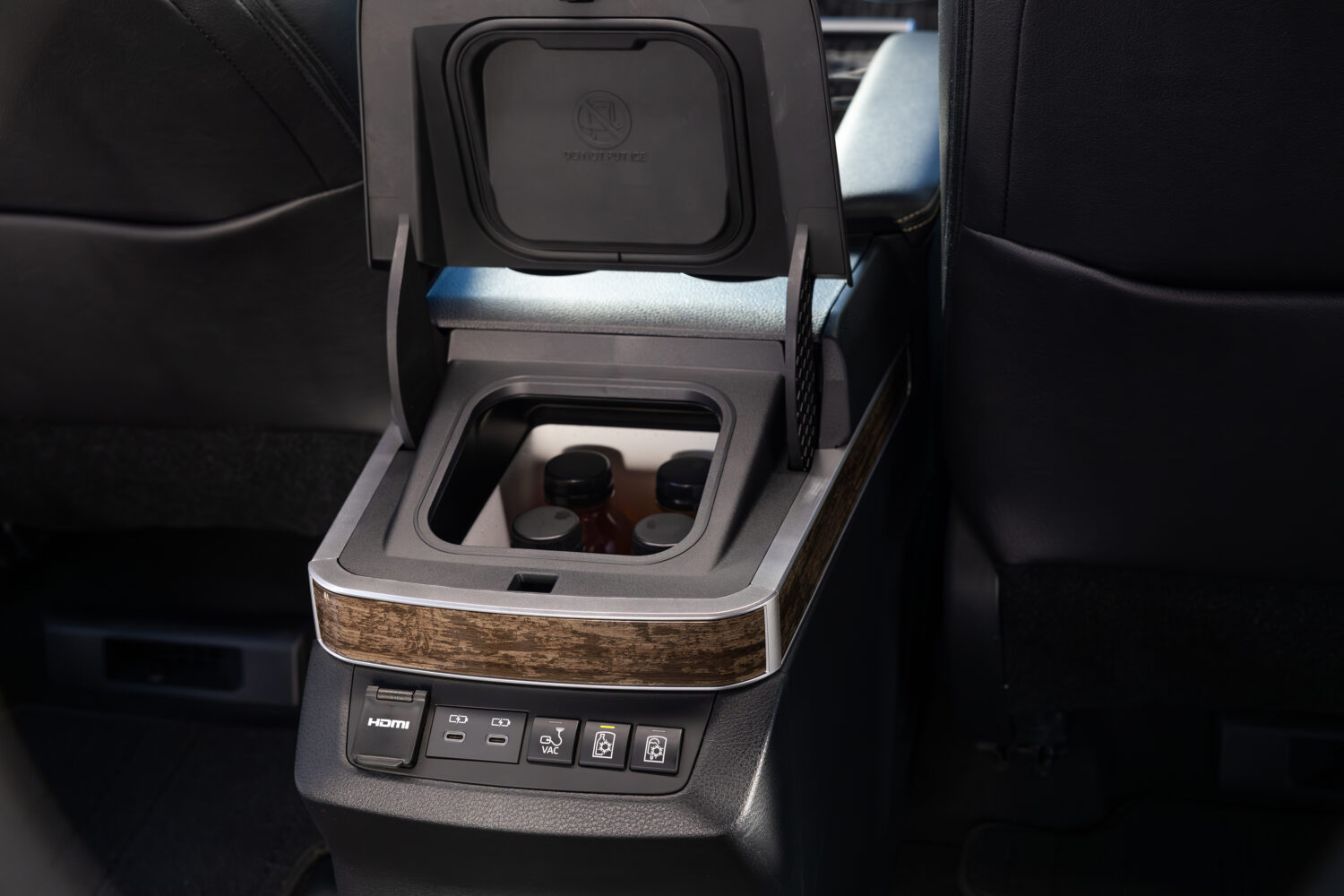 Interior center console of the 2025 Sienna Platinum AWD showing the built-in FridgeBox with drinks inside and woodgrain trim finish.