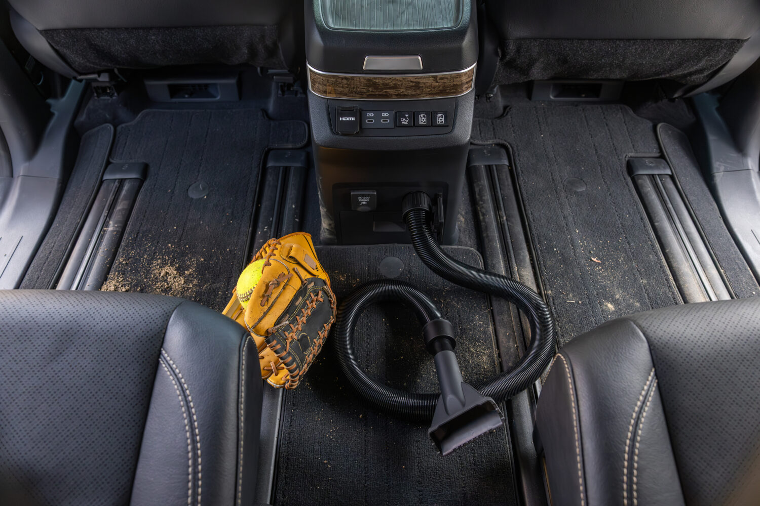 Built-in vacuum system of the 2025 Toyota Sienna Platinum shown cleaning up dirt and a softball glove between the second-row seats.