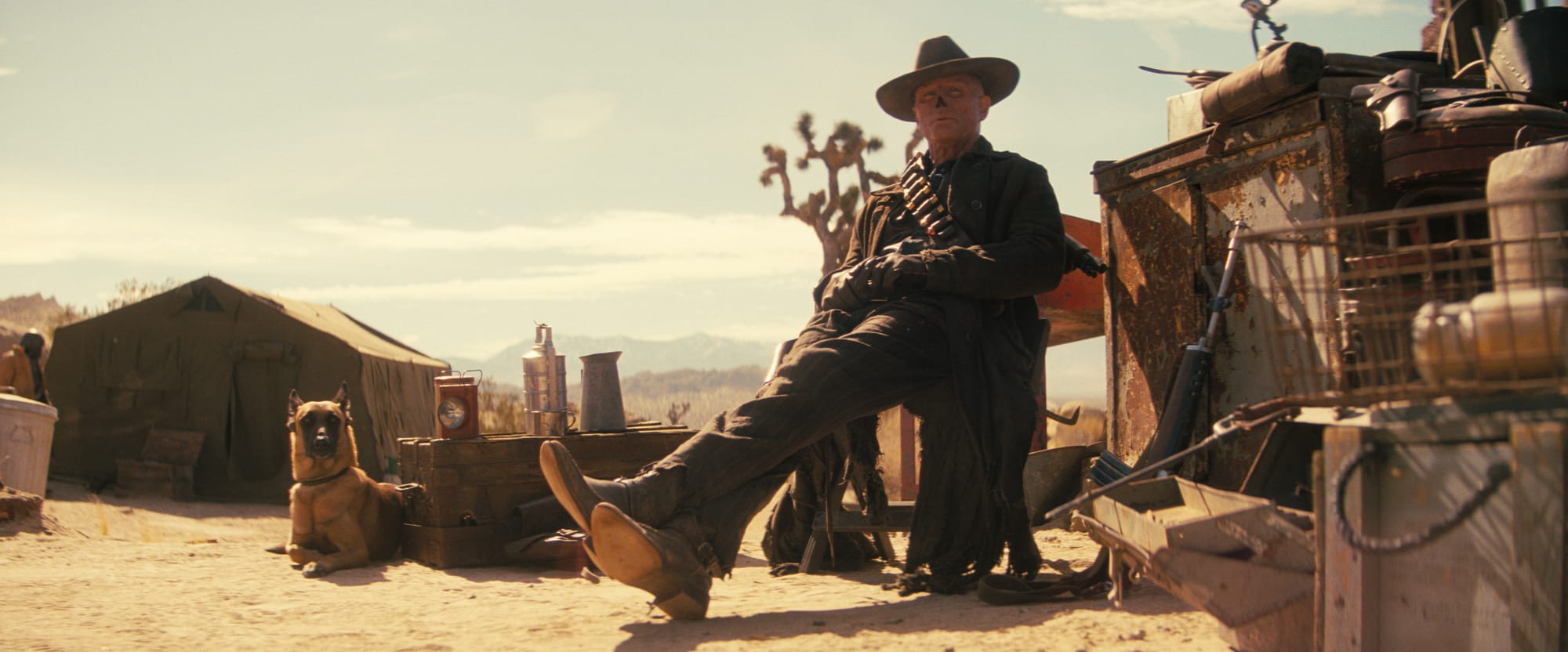 Fallout parents guide scene featuring the Ghoul resting in the desert wasteland with survival gear and weapons