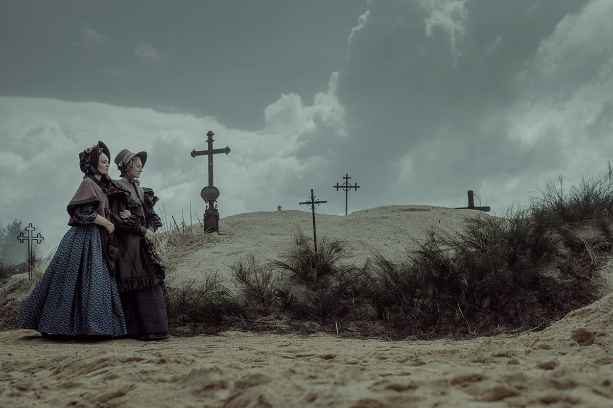 Ellen Hutter and Anna Harding (Emma Corrin) standing in a desolate, wintry 19th-century cemetery, capturing the gothic horror atmosphere of Robert Eggers' Nosferatu. 