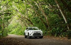 2026 Toyota Grand Highlander Hybrid MAX Platinum driving on a wooded road exterior view