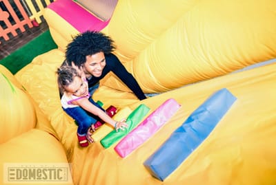 Latin american dad playing with mixed race daughter on inflatable slide at kindergarten playroom