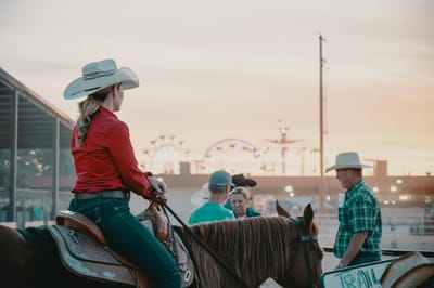 A female cowboy on horseback participates in a lively rodeo at sunset.