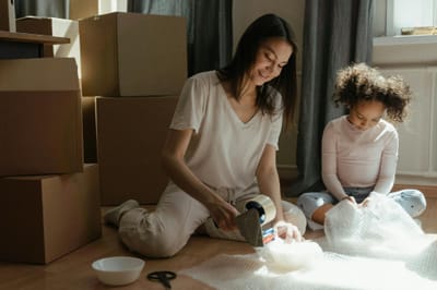 A mother and daughter packing boxes while preparing for a move in a sunlit room.