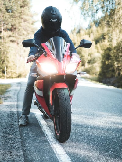A motorcyclist wearing a helmet rides a red sports bike on a scenic forest road.
