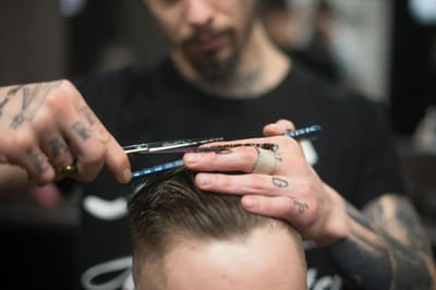 A tattooed barber provides a precise haircut in a modern barbershop setting.