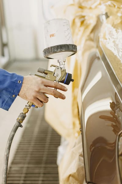 A technician spray paints a car with a paint spray gun in a workshop.