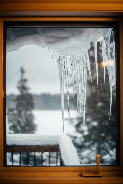 A view of icicles hanging from a window frame on a snowy winter day.