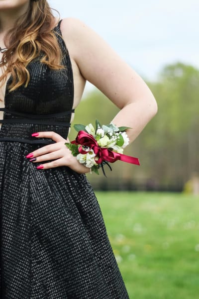 A woman's hand wearing a corsage on a black dress in an outdoor setting.