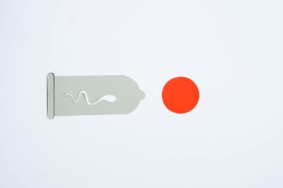 Abstract representation of fertilization with a condom and sperm on a gray background.