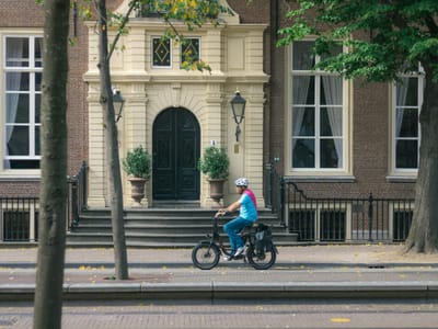 Adult cyclist wearing helmet rides through city street past historic building.