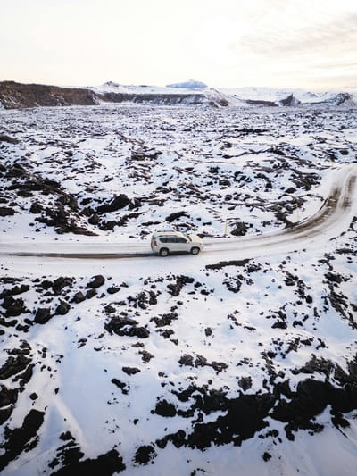 Aerial view of an SUV navigating a snowy Icelandic landscape, capturing winter's serene isolation.