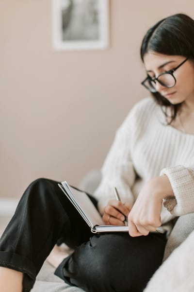 Attentive female wearing eyeglasses and casual outfit sitting barefoot with crossed legs on comfortable couch in modern flat