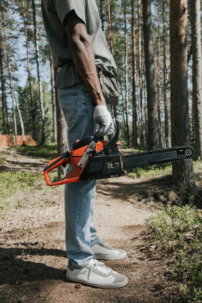 Close-up of an arborist holding a chainsaw in a wooded area.