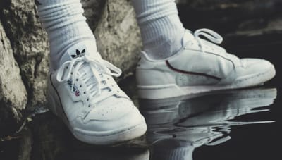 Close-up of white sneakers and socks reflecting on water next to a rock.