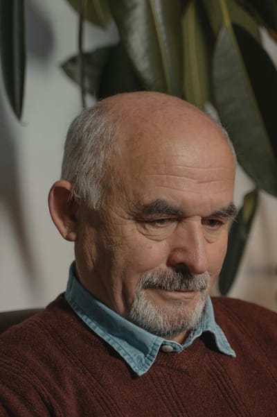 Close-up portrait of a thoughtful senior man with white hair and a goatee indoors.