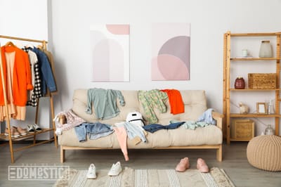 Messy pile of clothes on sofa and shoes in living room