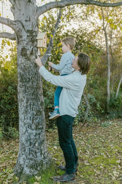 Father and son bonding while installing a birdhouse on a tree outdoors.