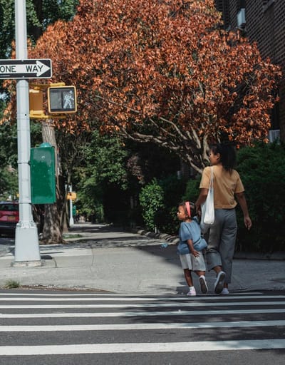 Full body back view of Asian anonymous mother with bag and little girl holding hands while walking on crosswalk on street