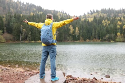 Photo happy man spreads hands to sides enjoying wild nature while hiking tourist with backpack stands