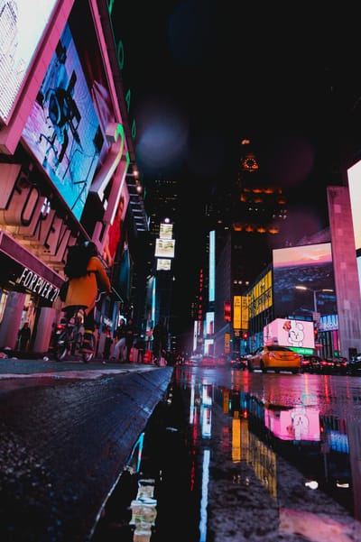 Illuminated street scene of Times Square with neon lights and reflections at night in NYC.