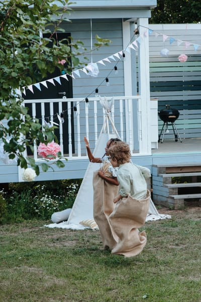 Kids having fun with a sack race near a decorated bungalow, a joyful outdoor celebration.