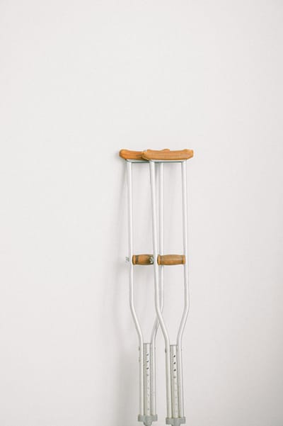 Minimalist image of crutches leaning on a white wall indoors.