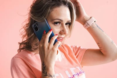 Smiling woman with tattoos chatting on smartphone in a bright studio setting.
