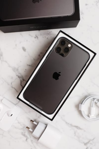 Top view of black mobile phone with multiple lenses in opened box with accessories on marble table