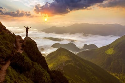 Photo wide mountain panorama. small silhouette of tourist with backpack on rocky mountain slope with raised hands over valley
