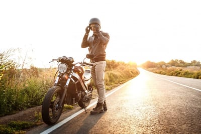 Young handsome man posing near his motorbike at countryside road.