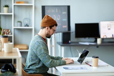Young male employee or designer sitting by desk in front of laptop in office and analyzing online da