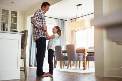 Father and young daughter smiling together in a bright kitchen, representing a safe and secure home environment for kids.